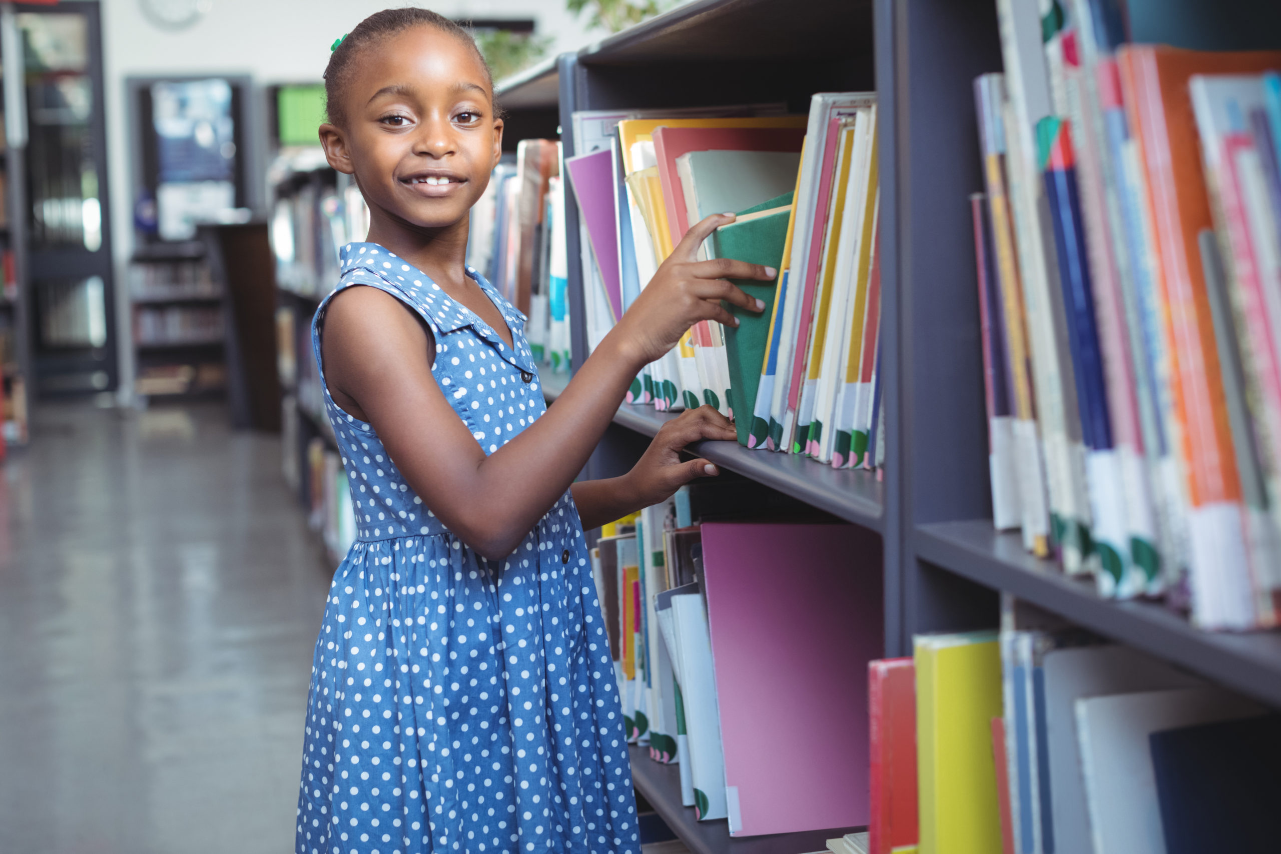 Portrait of girl selecting book from bookshelf in library