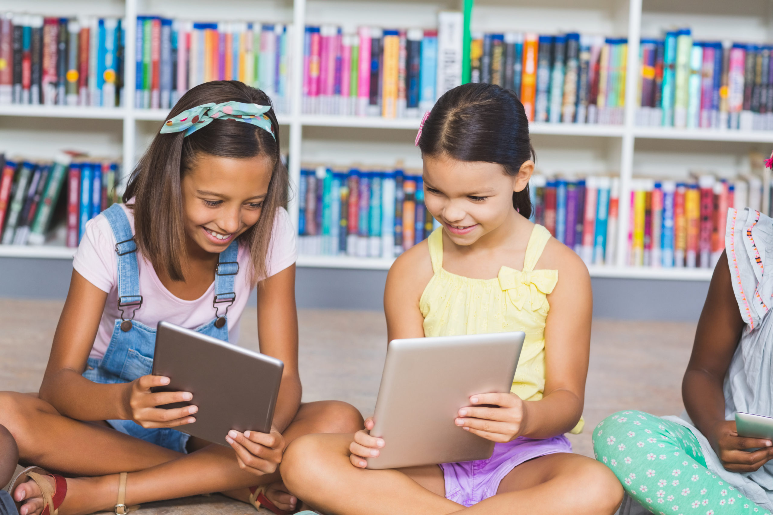 School kids sitting on floor using digital tablet in library at elementary school