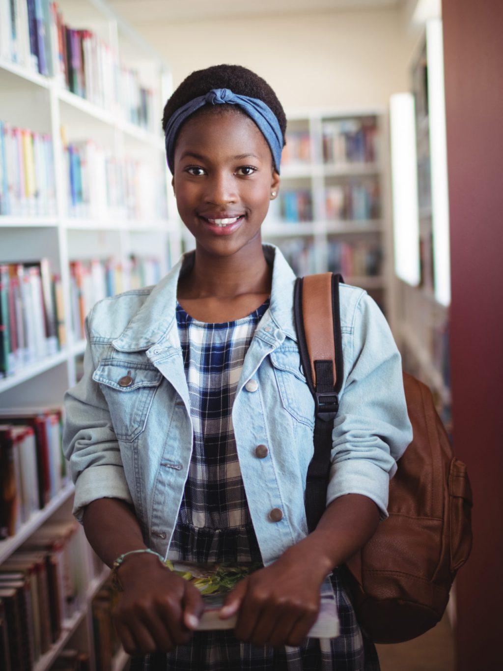 Portrait of schoolgirl standing with books in library at school